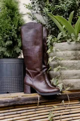 Bota de caña alta color marrón con textura símil reptil, taco cuadrado forrado en cuero y cierre lateral.