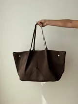 Bolso tipo tote de neopreno en color marrón, con diseño estructurado y costuras decorativas. Cuenta con doble asa de hombro en color contrastante y detalles de broches metálicos en los laterales.
