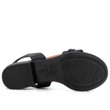 Sandalia de cuero negra con elástico en el tobillo, taco bajo y hebilla decorativa.