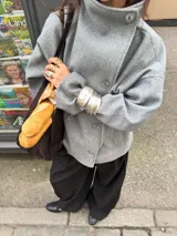 Chaqueta de paño color marrón oscuro, con diseño de doble botonadura frontal y cuello alto estructurado. Presenta mangas largas y un corte recto y holgado.