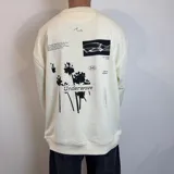 Buzo color crema de corte oversize con cuello redondo y puños acanalados. Presenta estampados en negro con motivos de palmeras, calamar, texto y logo de la marca.