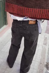 Jean de corte recto y tiro medio, confeccionado en denim de color negro lavado. Presenta costuras verticales en el frente y la parte trasera, y bolsillos posteriores con un bordado de brújula. Incluye una etiqueta de cuero con el logo de la marca en la cintura.
