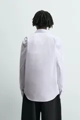 Camisa slim fit blanca con rayas verticales finas en color gris, confeccionada en tejido de algodón. Presenta cuello italiano y manga larga con puño abotonado. Cierre frontal con botonadura.