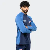 Buzo de entrenamiento Umbro del Club Nacional de Football, con medio cierre frontal, mangas largas y diseño en bloques de color azul y azul marino. Cuenta con el logo de la marca y el escudo del club en el pecho.