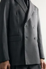 Blazer regular fit de Zara confeccionada en 100% lana, de color gris con diseño de rayas diplomáticas. Presenta cuello con solapas de pico, manga larga con botones en los puños, bolsillos con solapa en la cadera y bolsillo de vivo en el pecho. Cuenta con cierre frontal de botonadura cruzada.