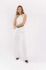 Conjunto de dos piezas color blanco compuesto por un chaleco sin mangas con diseño cruzado y un pantalón de vestir de corte recto. El chaleco incluye un cinturón fino negro con hebilla dorada que marca la cintura.