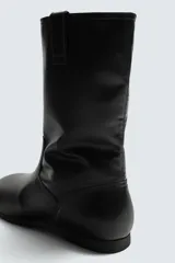 Bota de caña media fabricada en piel lisa, con diseño minimalista, tiradores laterales y suela a tono con ligero tacón.