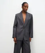 Blazer de sastrería color gris oscuro, con cuello solapa, cierre frontal de un botón y bolsillos laterales con tapa. Presenta un diseño estructurado con mangas largas y forro interno.