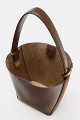 Bolso tipo saca con diseño estructurado, confeccionado en una combinación de cuero liso y gamuza en tono marrón. Cuenta con asa de hombro fija, cierre imantado y detalles metálicos en dorado.