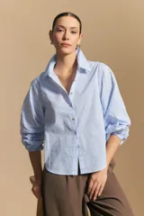 Camisa a rayas azules y blancas, de manga larga con puños elastizados, entallada en la cintura para definir la silueta.