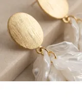 Caravanas de acero con baño de oro, compuestas por un disco superior metálico y un dije inferior con pétalos de resina blanca en forma de flor.