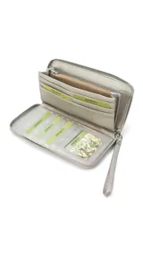 Billetera larga con cierre perimetral, confeccionada en material sintético con estampado botánico de flores silvestres sobre fondo claro. Cuenta con múltiples compartimentos internos para tarjetas, visor para documentos y un bolsillo interno con cierre. Incluye una correa de mano extraíble.