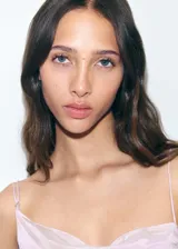 Vestido corto de satén en color lila, con diseño entallado y cuello asimétrico. Presenta tirantes finos, detalle de fruncido lateral con lazo ajustable y una pequeña abertura en el bajo. Cuenta con espalda abierta y forro interior.