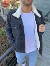 Chaqueta de jean color negro con interior y cuello de corderito sintético blanco. Presenta cierre frontal con botones metálicos y bolsillos frontales con solapa.