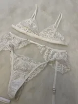 Conjunto de lencería compuesto por bralette de encaje con breteles regulables, tanga regulable y portaligas con volados en la cadera y ligas incorporadas.
