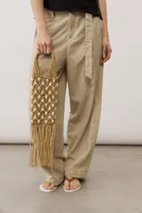 Cartera de mano tipo red confeccionada en tejido de macramé color crudo, con aplicaciones de cuentas blancas y detalles de flecos colgantes en la parte inferior. Cuenta con manija de mano integrada.