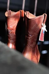 Botas tejanas de cuero negro con punta cuadrada y tacón bajo. Presentan bordados rojos de estilo western en la caña.