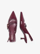 Zapatos slingback de cuero sintético acharolado color bordó, con punta fina, taco bajo y tiras cruzadas en el empeine con hebilla metálica dorada.