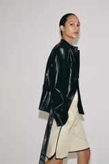 Cazadora efecto piel de Zara Woman Collection, en color negro. Cuenta con cuello redondo, manga larga, bolsillos de parche con solapa en el delantero y cierre frontal con botones forrados. Incluye un cinturón del mismo tejido para ajustar en la cintura.