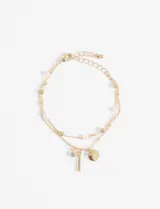 Pulsera dorada de doble cadena, una con cuentas cuadradas y otra con perlas. Incluye dijes colgantes: un cristal, una barra y un círculo.