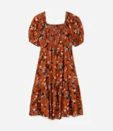 Vestido corto color ladrillo con estampado de flores y palmeras en tonos blanco y negro. Tiene escote cuadrado, mangas cortas abullonadas y falda con volantes.