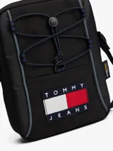Cartera reporter de estilo urbano color negro, con compartimento principal con cierre, cordones elásticos ajustables en el frente y correa ajustable. Presenta el logo de la marca en un parche frontal y etiqueta lateral de Cordura.