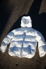 Campera puffer blanca con capucha y logo reflectivo en el pecho.