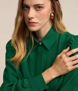 Camisa de crepé color blanco, con cuello inglés, manga larga abullonada con puños abotonados y cierre frontal oculto con botón diferenciado en el cuello.