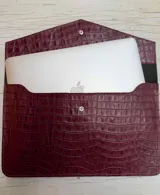 Funda para laptop de diseño minimalista, confeccionada en cuero negro con textura grabada tipo reptil y cierre mediante botón metálico a presión.