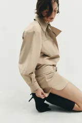 Vestido corto de cuello solapa y manga larga, con bolsillos delanteros y detalle de cinturón a tono. Presenta cierre frontal con cremallera oculta y bajo con aberturas laterales.
