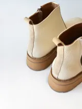Bota corta de cuero vacuno con textura granulada, color crudo. Presenta cierre lateral metálico, suela track de goma en tono suela y tirador trasero.