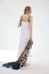 Vestido midi de lino color salmón, de corte amplio y silueta holgada. Presenta diseño con cortes irregulares y detalles de pasamanería en el escote y costuras. Cuenta con breteles dobles tipo cuerda y ruedo asimétrico.