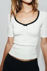 Camiseta blanca de manga corta y corte slim fit, con escote redondo ribeteado en negro, detalle de frunce en el centro del pecho y un pequeño lazo negro decorativo.