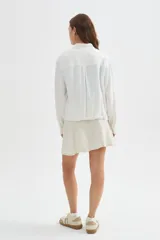 Chaqueta bomber blanca de algodón con cuello mao, bordado sutil, bolsillos frontales con solapa, cierre de botones y cordón ajustable en el ruedo.