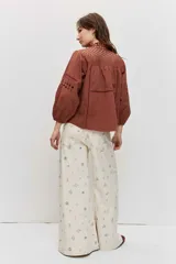 Camisa de manga larga abullonada color marrón, con detalles de bordados calados en el pecho y las mangas, y cierre frontal con botones.