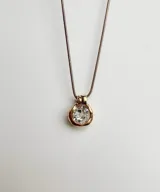 Collar plateado con dije circular con piedra transparente facetada. Cadena fina de eslabones.