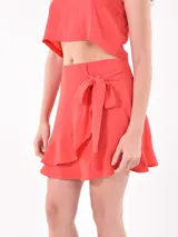 Falda corta tipo pareo color rojo, con detalle de lazo lateral y terminación con volado en el ruedo.