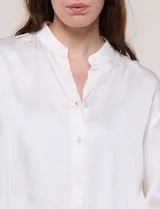 Camisa de satén azul marino con cuello mao, escote en V y mangas tres cuartos con hombro caído. Presenta silueta holgada, cierre frontal con botones y ruedo asimétrico.