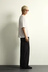 Camiseta de corte holgado con cuello redondo y manga corta. Presenta un diseño frontal con la frase New York Essence combinando tipografía cursiva y letras en bloque con efecto relieve.