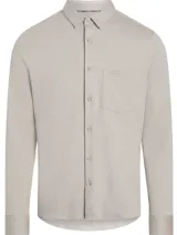 Camisa de manga larga color beige, corte slim, con cuello clásico, cierre frontal con botones, bolsillo de parche en el pecho y logo de Calvin Klein en el bolsillo.