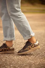 Zapatillas bajas con capellada de cuero negro y estampado animal print, con puntera redondeada, cordones negros y suela color caramelo.