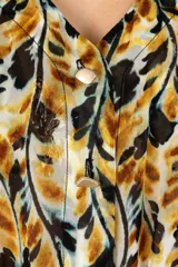 Cover up corto de estilo bohemio con estampado en tonos amarillos, naranjas y negros. Presenta un diseño de tela ligera y traslúcida con escote en V, botones frontales y mangas largas con puños elásticos. Incluye un cinturón de lazo ajustable en la cintura y un ruedo con terminación en volados.