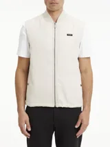 Chaleco blanco hueso acolchado, con cuello alzado de punto de canalé, cierre frontal con cremallera, bolsillos laterales con botón a presión y logo de Calvin Klein en el pecho.