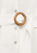 Vestido midi de lino color blanco, con cuello camisero, cierre frontal de botones, manga larga con puños abotonados y cinturón de tela con hebilla circular a tono.
