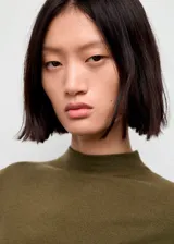 Vestido midi de tejido de punto fino en color verde oliva, con cuello perkins, manga larga y diseño entallado con fruncidos laterales.