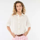 Camisa de corte holgado en color blanco, con cuello clásico, mangas cortas con dobladillo y cierre frontal con botones dorados en forma de estrella.
