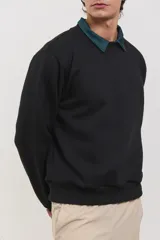 Buzo de algodón rústico color negro con cuello redondo y detalle de cuello tipo polo en color verde oscuro debajo. Presenta puños y ruedo acanalados, con un diseño de calce clásico.