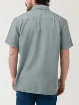 Camisa de manga corta RKF confeccionada en tencel, color verde grisáceo. Presenta cuello clásico, cierre frontal con botones claros, bolsillo en el pecho con bordado del logo del pato al tono y pinza en la espalda.