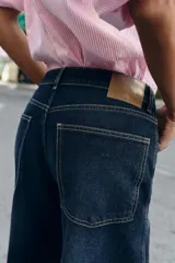 Jeans de tiro medio color azul oscuro, con cinco bolsillos, cierre de cremallera y botón. Presenta una silueta curvada, más ancha en el muslo y la rodilla, y un bajo con vuelta.