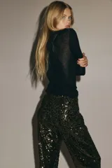 Pantalón de tiro alto confeccionado en malla revestida de lentejuelas brillantes. Presenta un corte bootcut y cuenta con forro interior de punto para mayor comodidad.